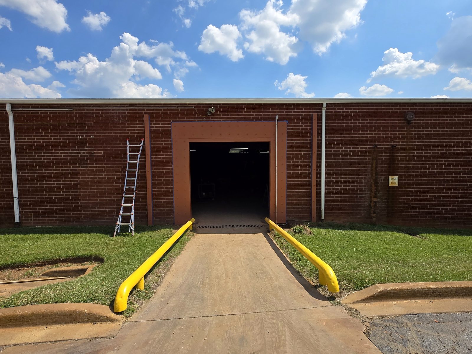 The finished new steel-framed door opening from outside, cut into the existing brick building with new bollards and ramp